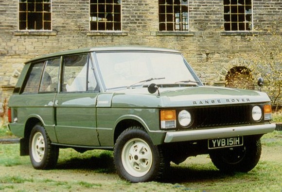 Green Mk1 Range Rover parked on grass in front of derelict building