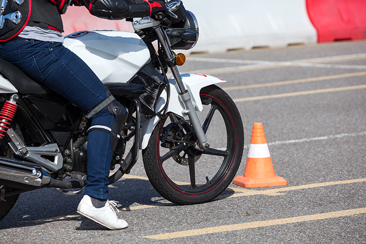 Learner motorcyclist riding a white bike around carpark. Small orange cone