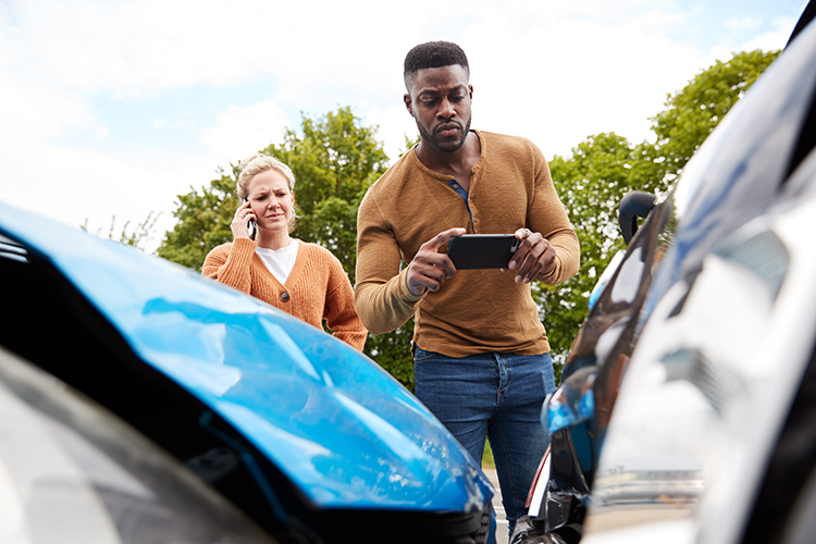 Male taking photo evidence of a car crash using smartphone. Female on phone stood behind him