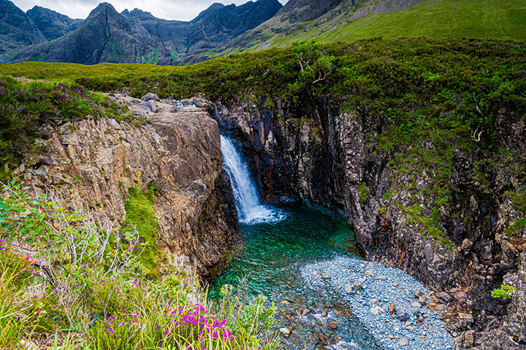 A waterfall surrounded by mountains and grass