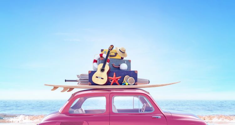 Red car on the beach with a sufboard, guitar and other luggage on the top 