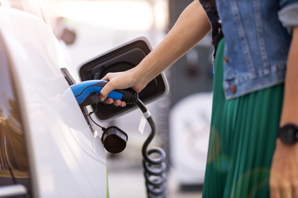 A close up of a womans hand holding the charger as it charges her electric vehicle 