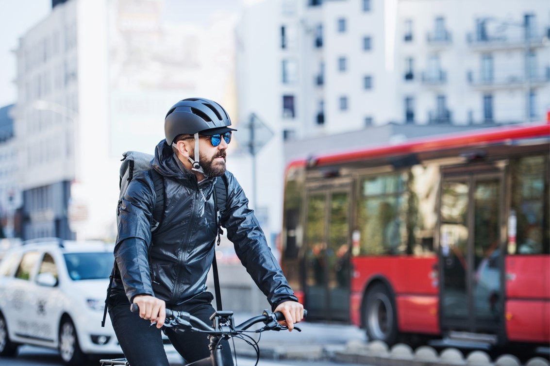 Man riding a bike in the city with a helmet and sunglasses on. Red bus in background