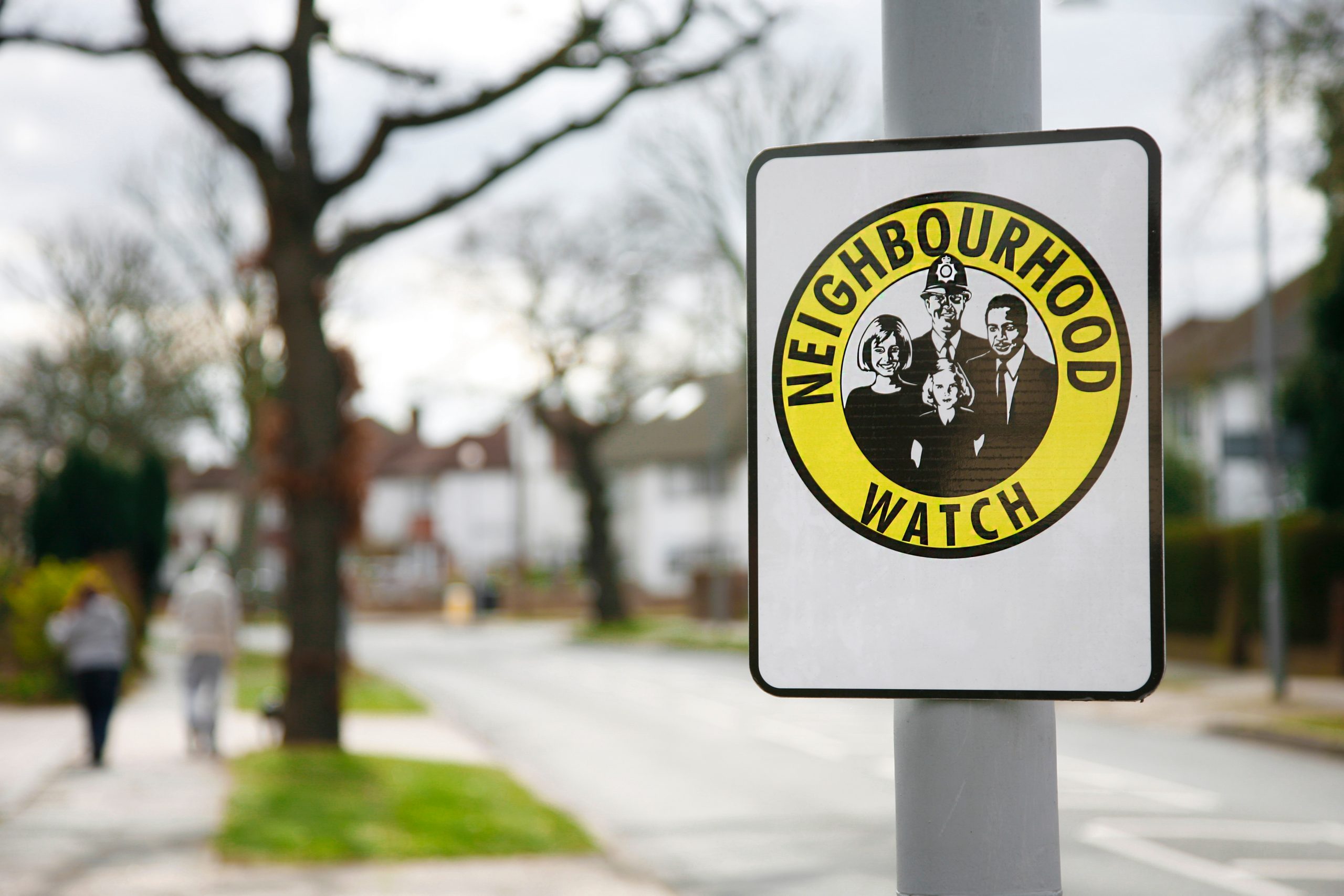 A yellow Neighbourhood watch sign on a lamp post in a residential area