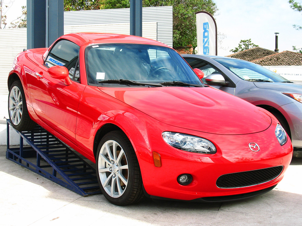 Red Mazda MX-5 Cabriolet on a stand at a car dealership parked next to a silver vehicle