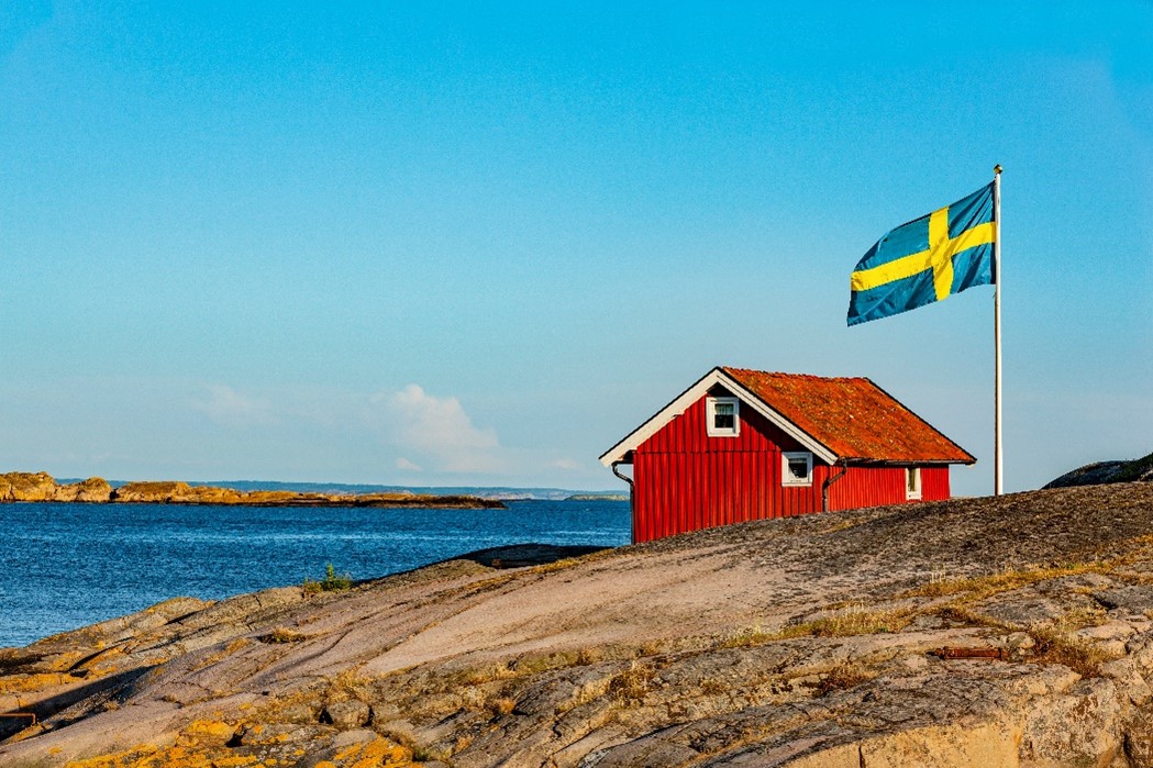 Swedish flag next to a small red building beside the sea