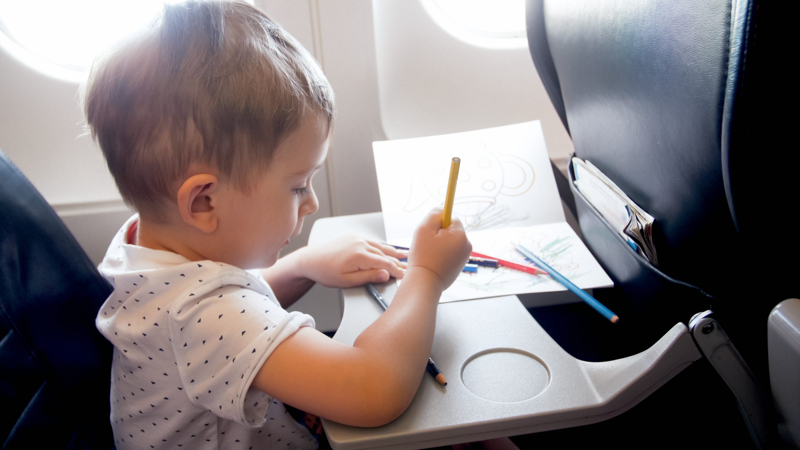 Toned portrait of little boy traveling by plane and drawing with pencils 