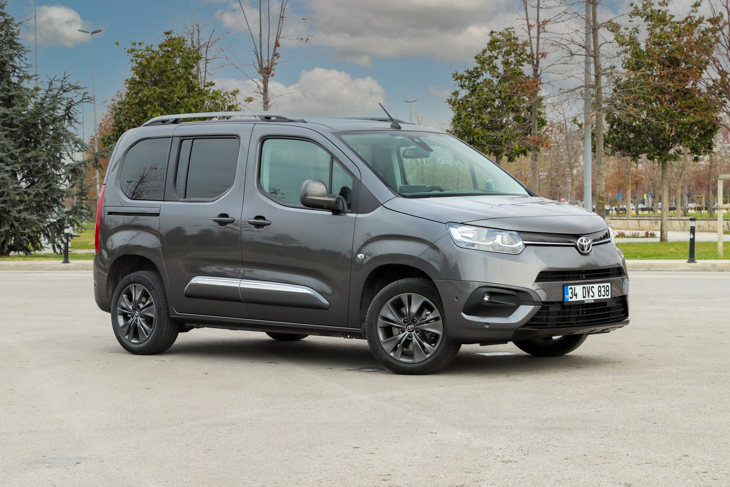 A grey van/ people carrier vehicle parked in front of a woodland area