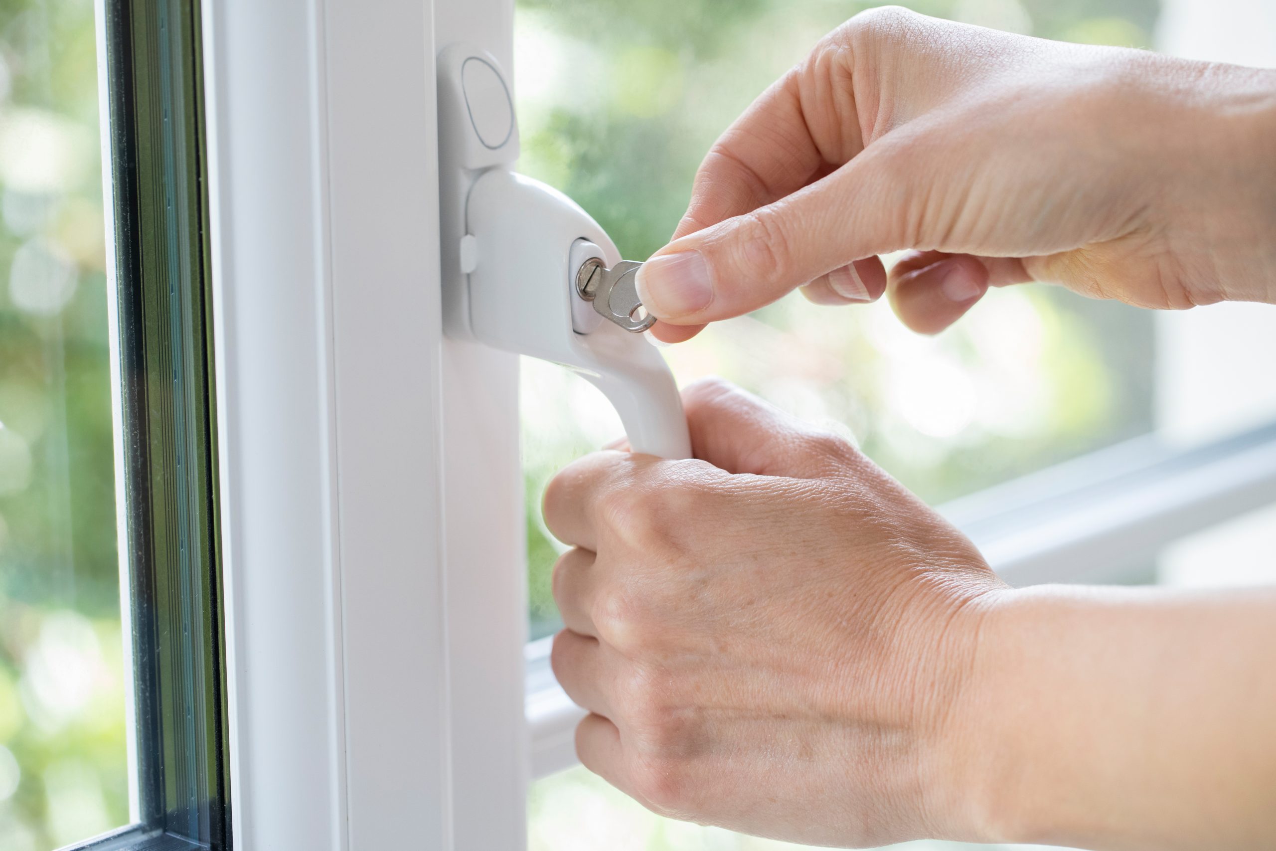 hands twisting a key in a window handle. Locking a Window 