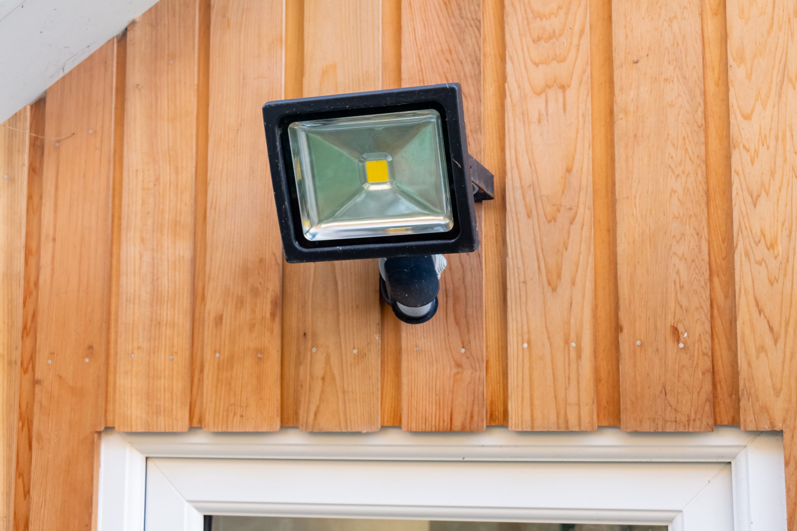 Garden flood sensor light fixed to a wooden wall above a door