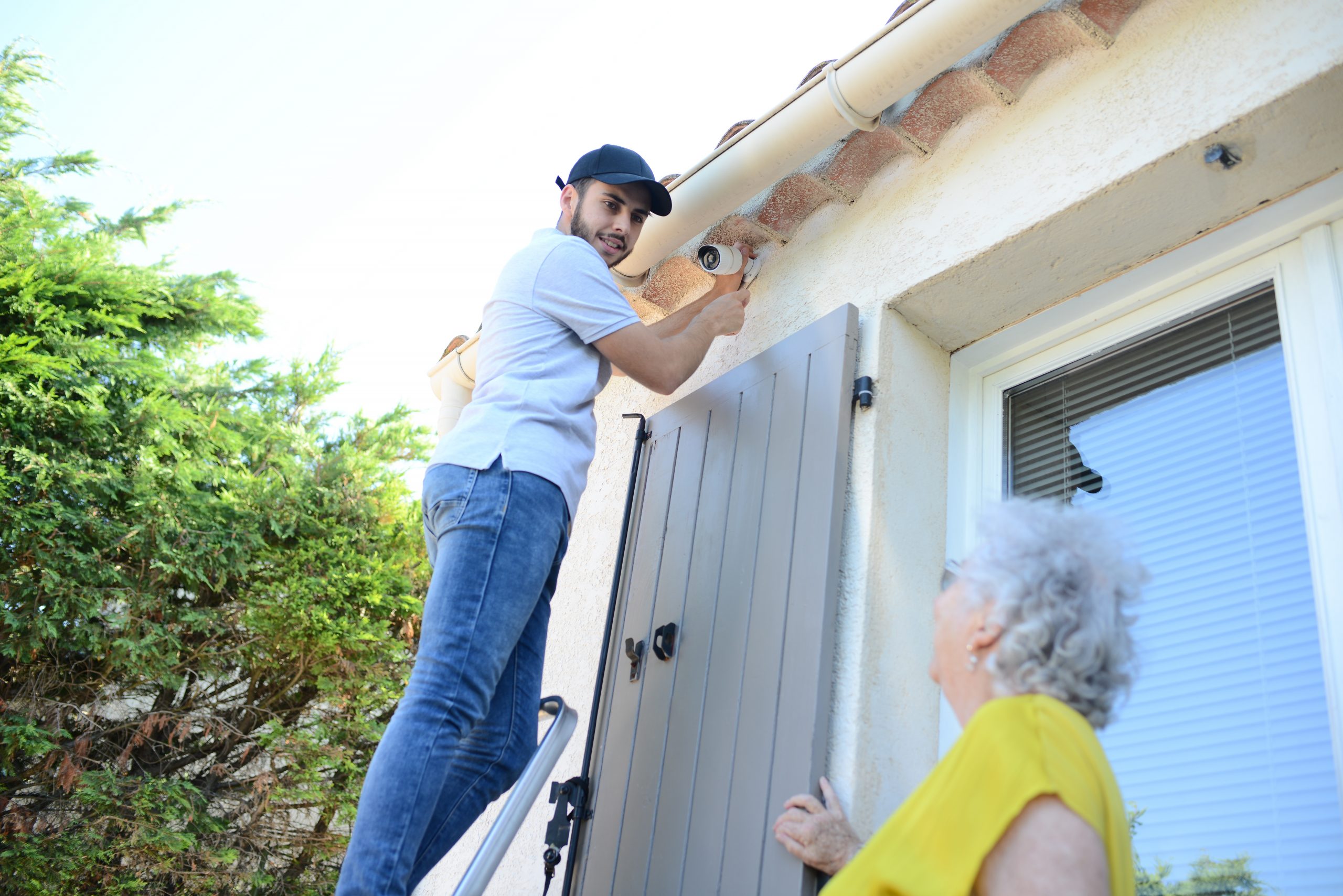 handsome young man installing house security anti burglary camera and siren alarm in a senior woman home