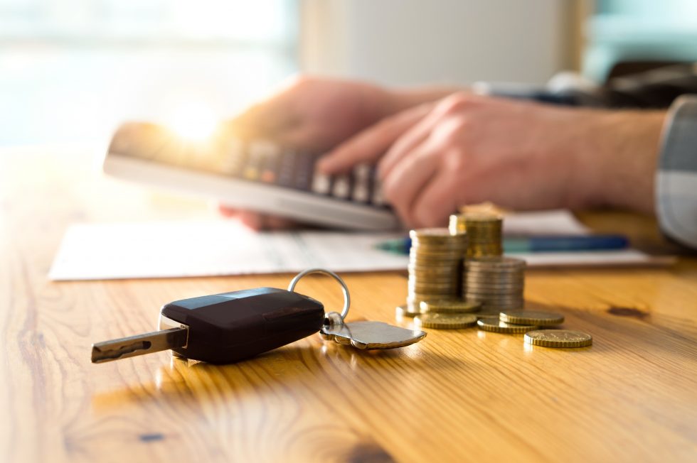 Male using a calculator to would out finances with a stack of coins and car keys