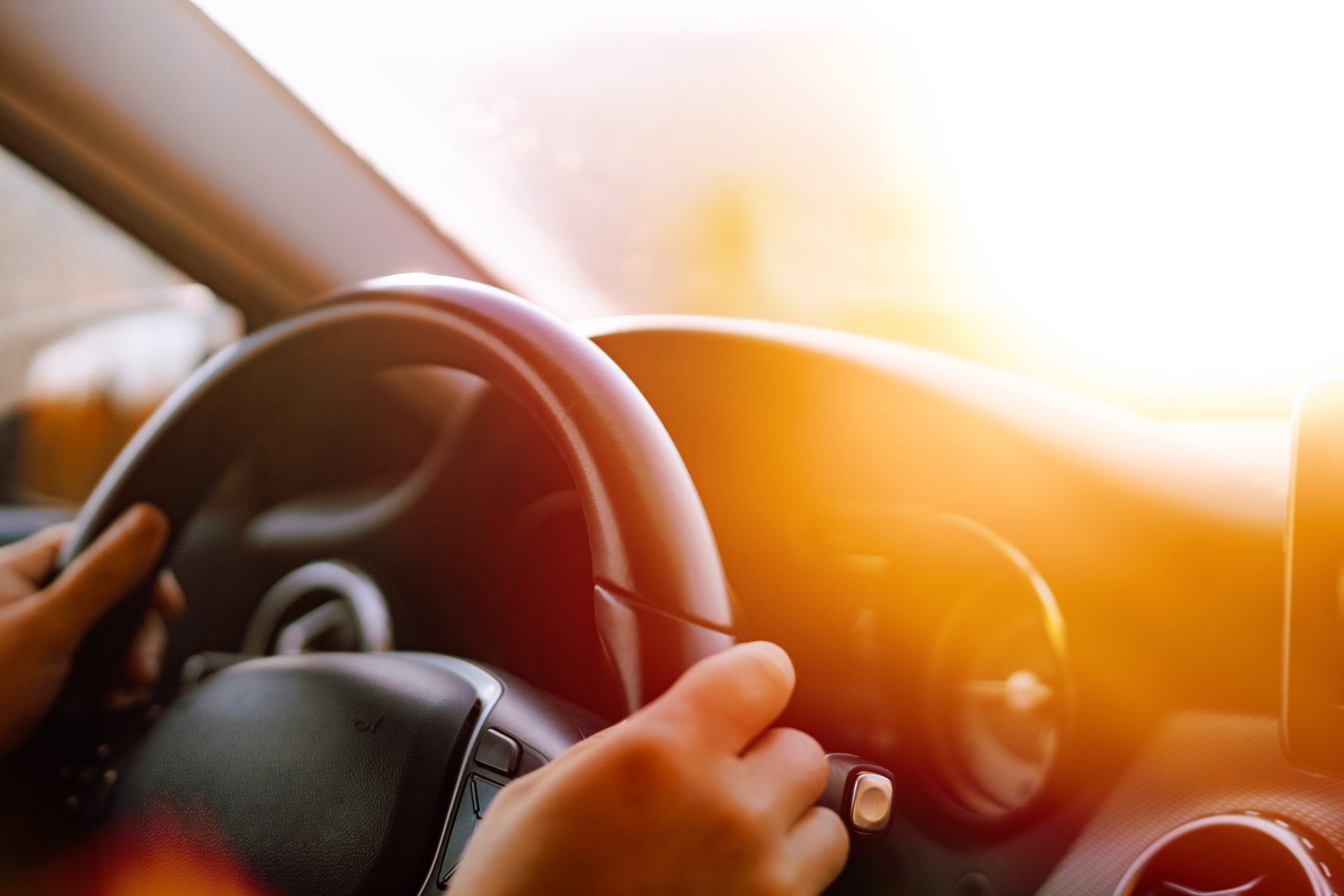 Close up of driver hands driving in road trip while the sunset is reflecting on the windscreen