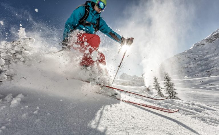 low angle show to a skier in a blue coat and red trousers skiing through snow