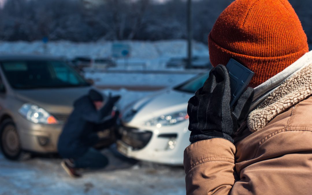 Crash between 2 vehicles in snow. one male crouched looking at damage with a close up of another person wrapped up in a hat and gloves on he phone