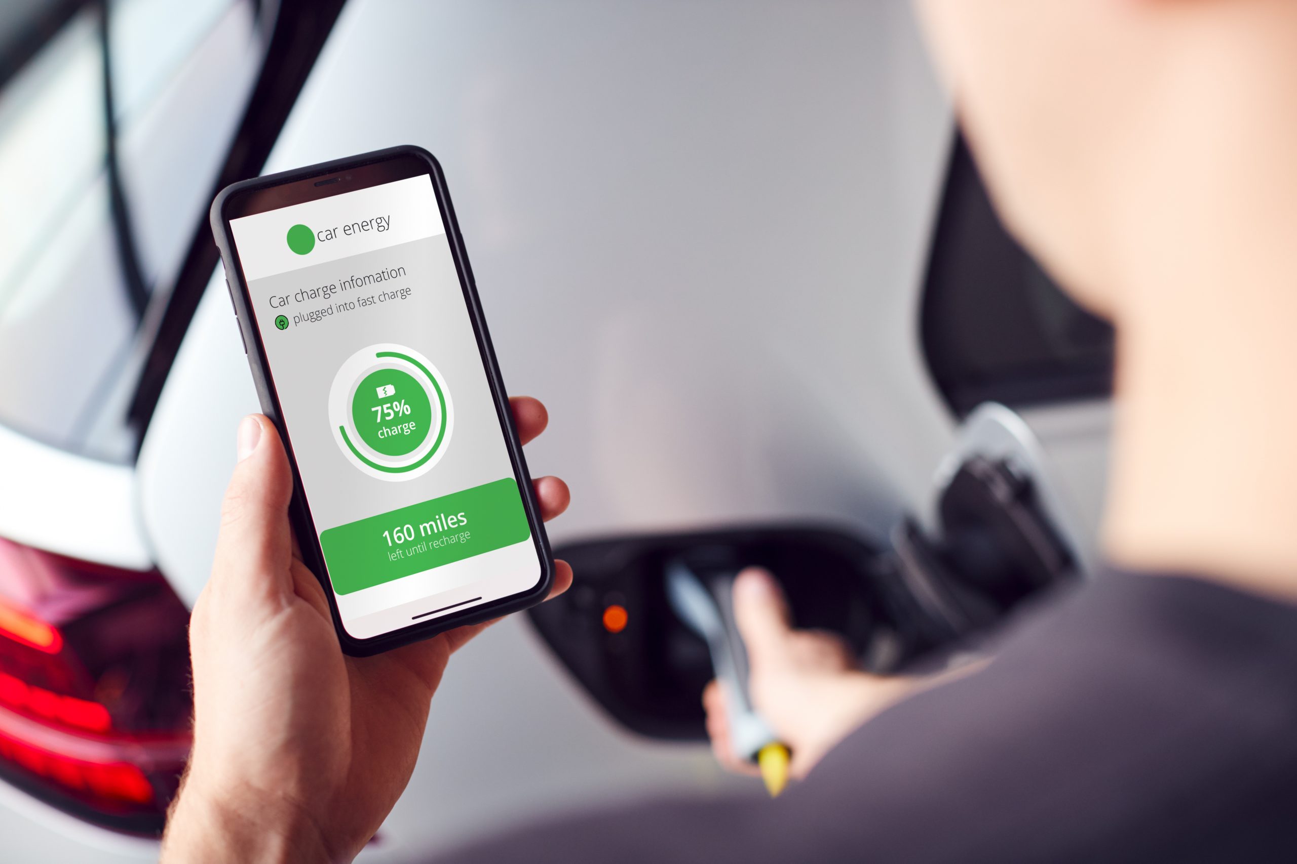 Man Charging Electric Vehicle With Cable Looking At App On Mobile Phone