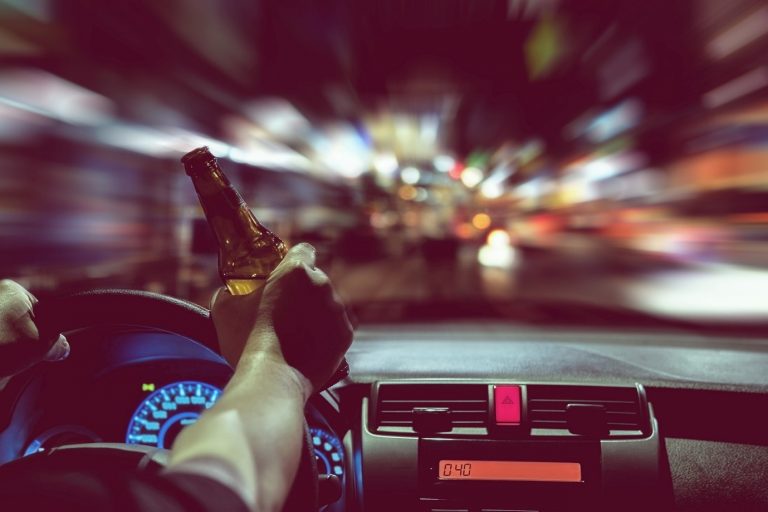 A POV a male driving with a brown glass beer bottle and a blurred road ahead .
