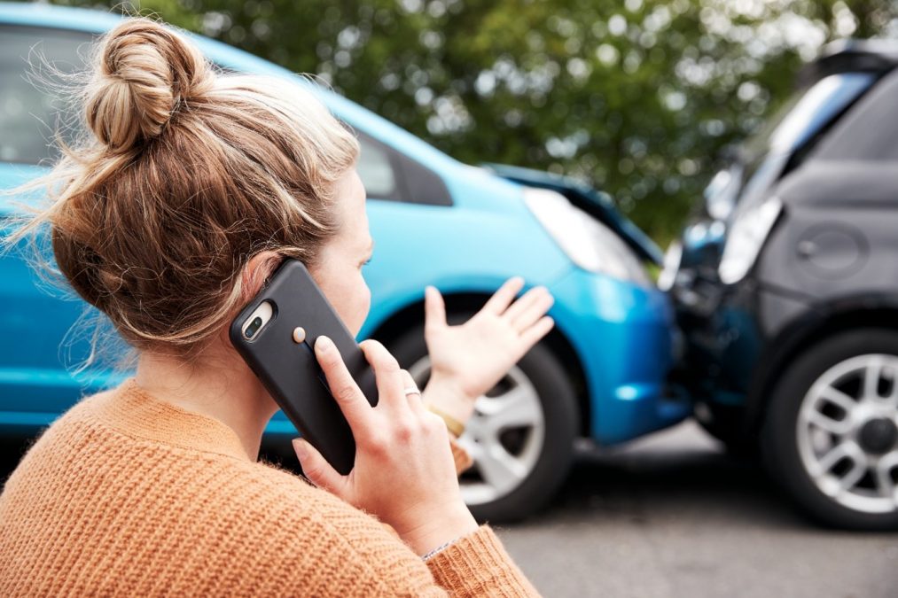 Lady on phone Infront of a blue car that has crashed into the rear of a black car