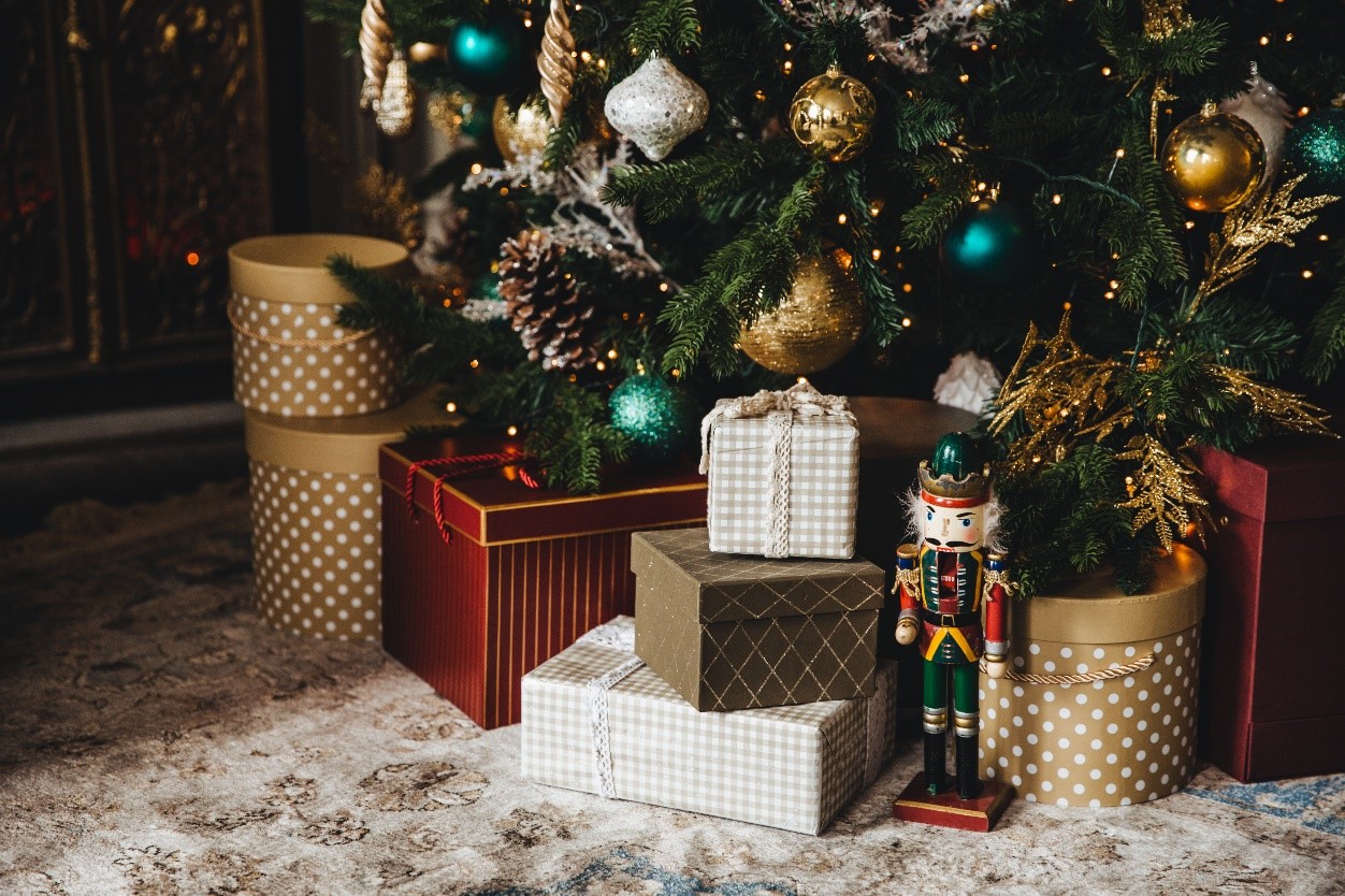 Wrapped up gold and white boxed presents under a green Christmas tree.