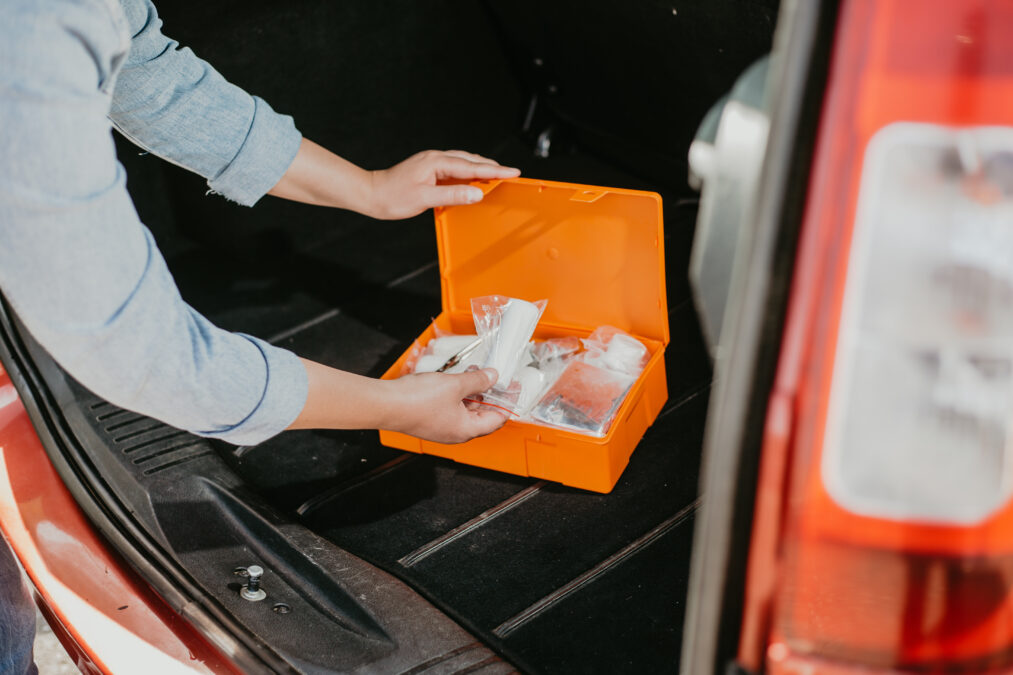 Young woman using car first aid kit box with kind of medical aids, transport concept