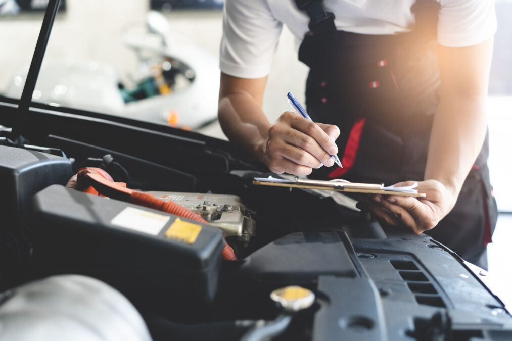 Auto check up and car service shop concept. Mechanic writing job checklist to clipboard to estimate repair quotation to client at workshop garage.