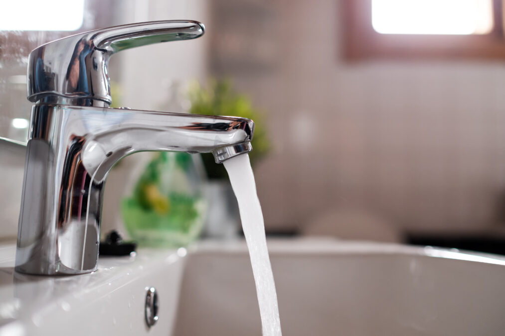 A silver lever bathroom tap with water flowing out into a sink