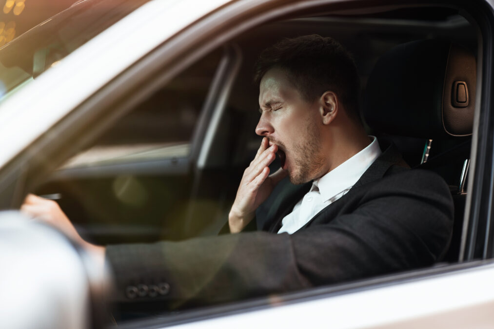 Man yawning while driving car, showing his tiredness
