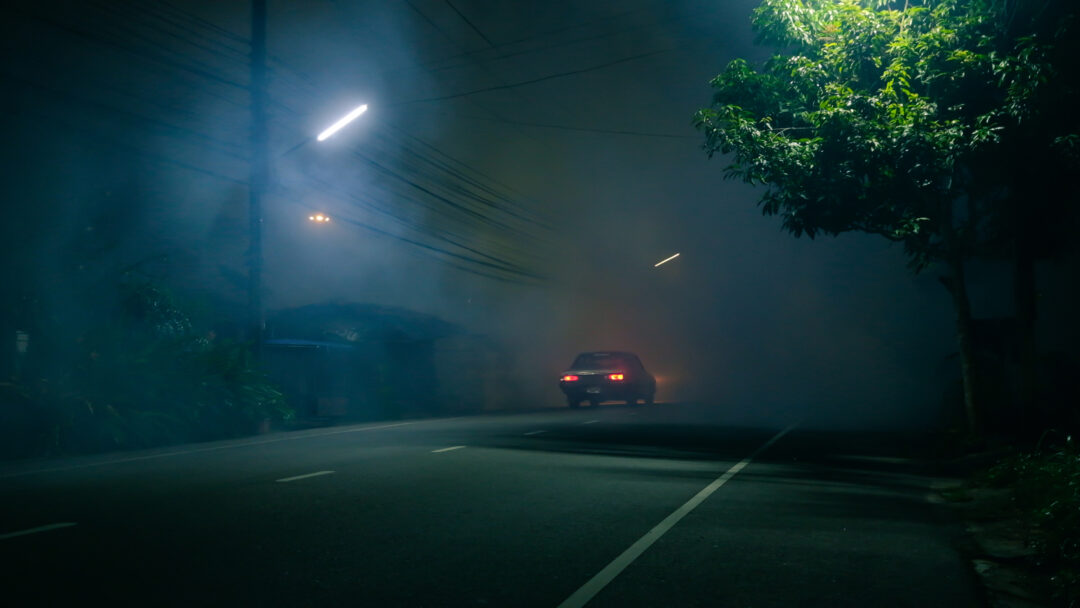 Car driving down road in fog with minimal lights on