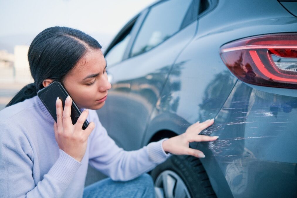A woman inspecting a scratch to the rear of her car whilst on the phone