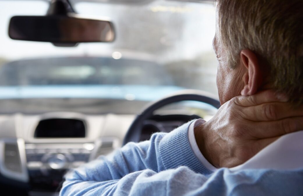 A man in a car holding his neck because of whiplash