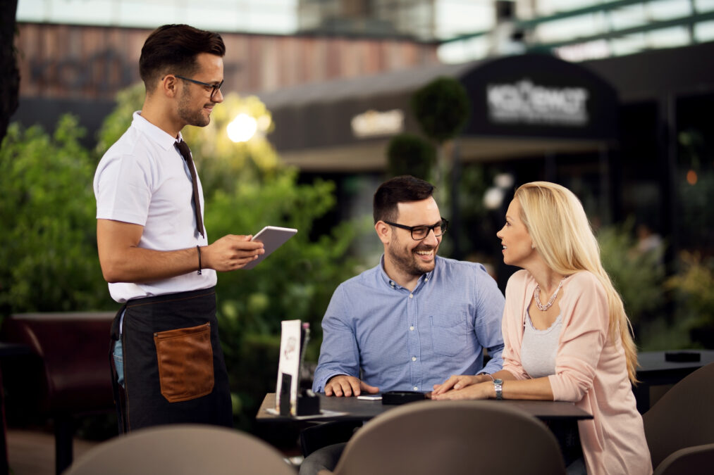 Couple speaking to waiter to order food at an outdoor restaurant