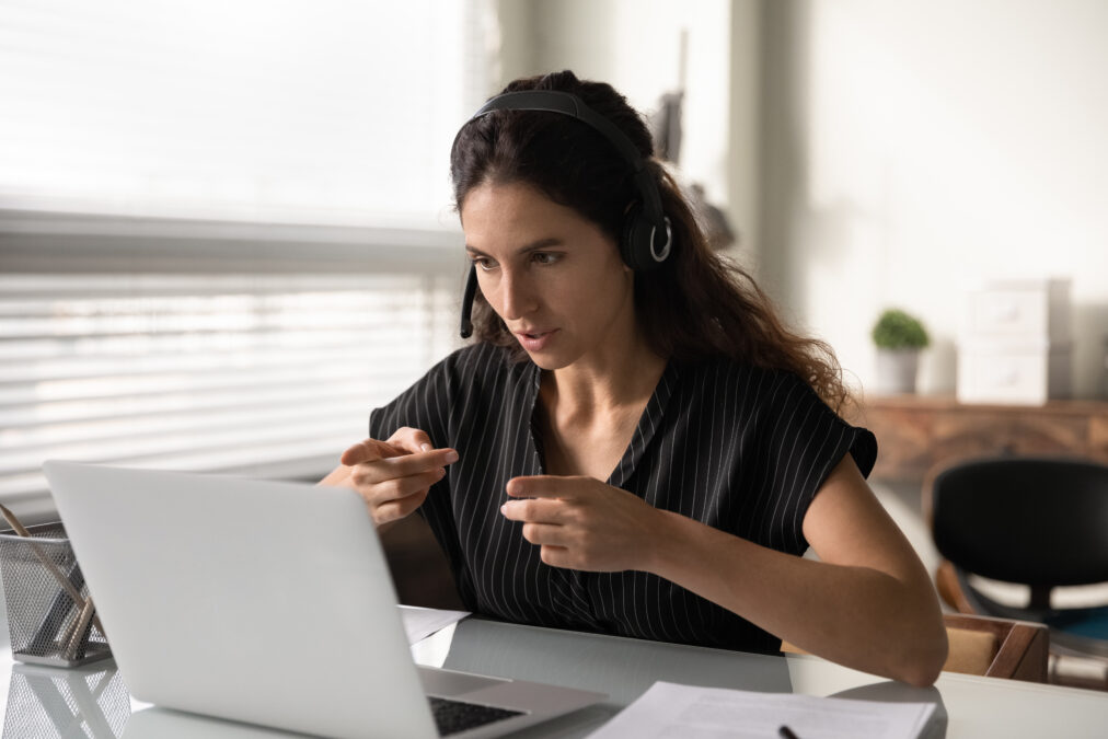 Female with dark hair wearing a head set speaking to someone via video webchat