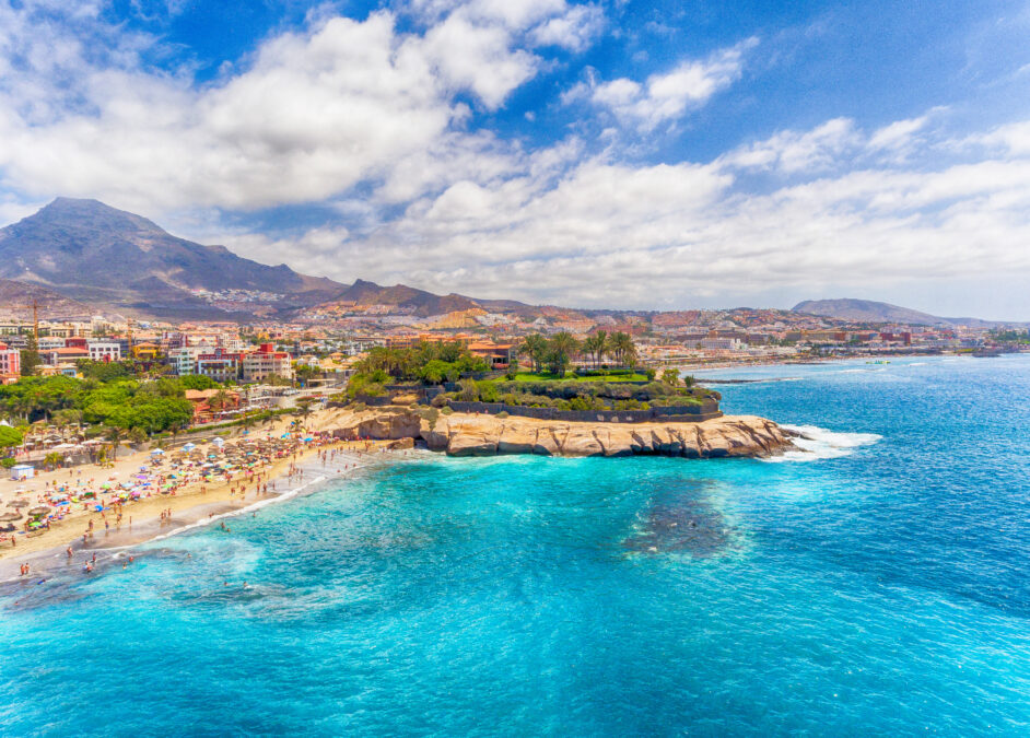 El Duque Beach aerial view in Tenerife, Spain. Crystal blue water with a mountain in the distance