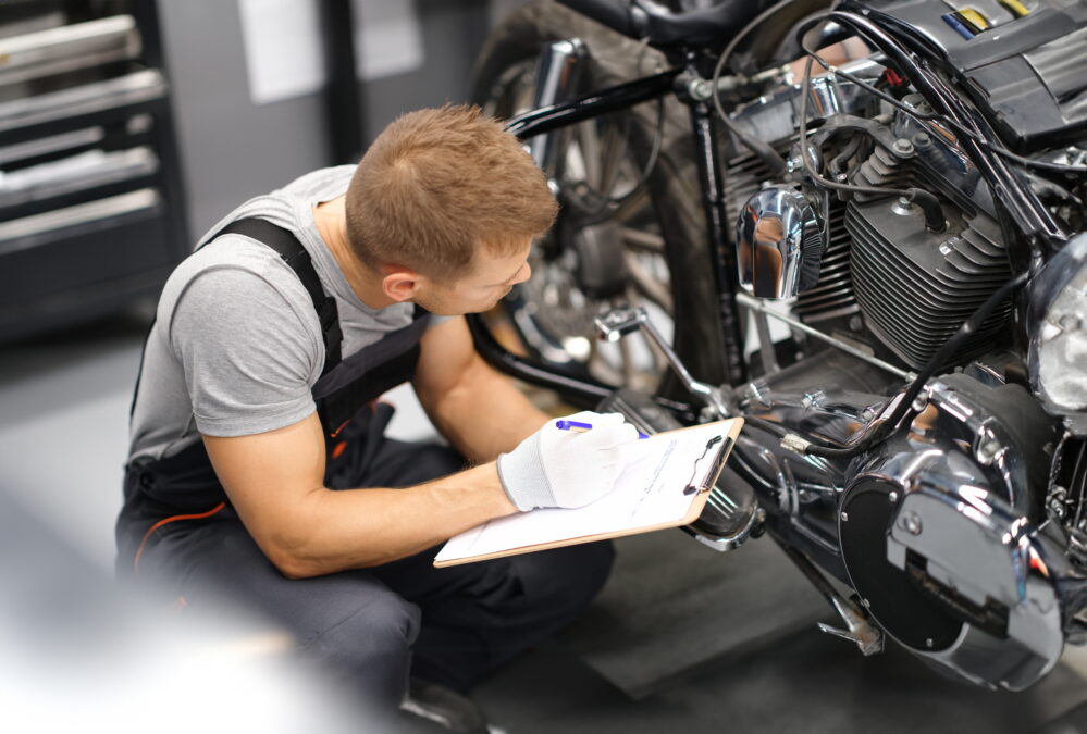 Mechanic  crouched down inspecting motorbike with a pen and clipboard