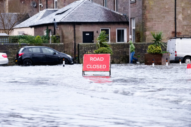 Road closed sign in flooded road with house and car behind it
