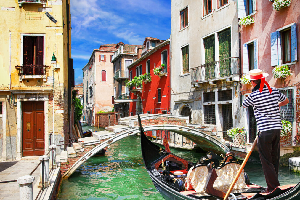 male in a black and white striped t-shirt rowing a gondola through the Venice canals 