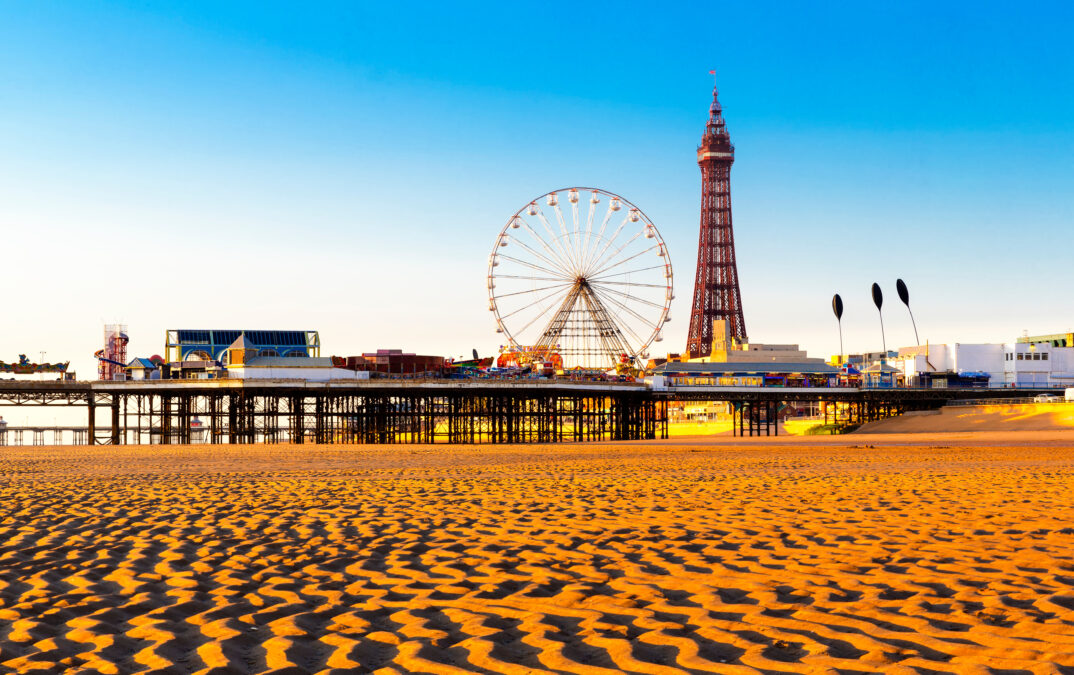 Blackpool Tower and Central Pier Ferris Wheel, Lancashire, England. Orange rippled sandy with the Blackpool pier full of the ferris wheel and tower up against the blue sky. 