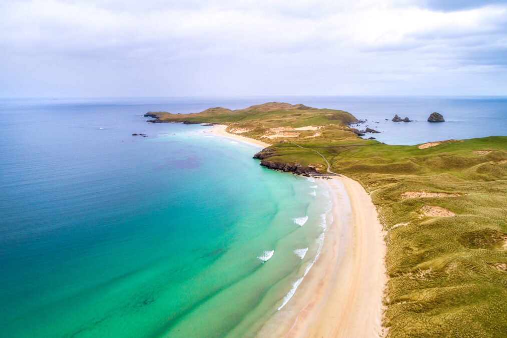 The beach of the peninsula Balnakeil. Crystal greeny blue waters and a green sandy hill.