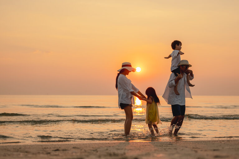 Happ family of 4 playing in the water on the beach at sunset