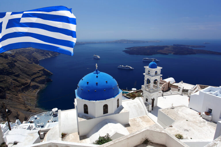 Greek flag over white and blue buildings overlooking the sea
