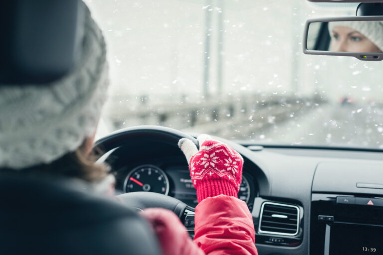 Woman in the red jacket, hat and christmas gloves is driving on the highway at the winter snowfall. View from the back seat of the car. concept.