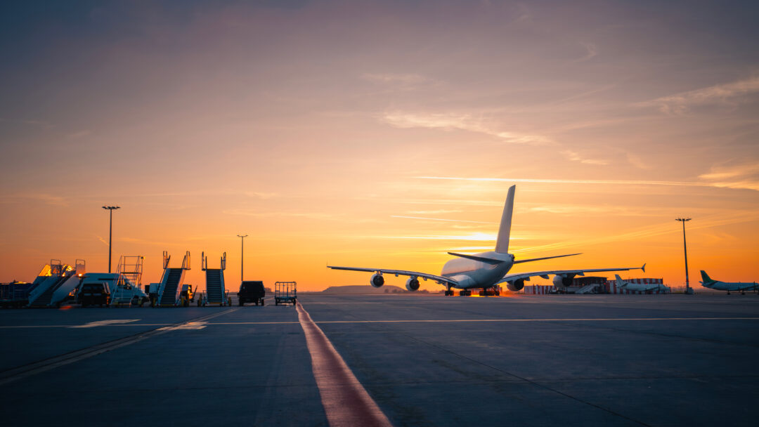 Traffic at airport at golden sunset. Wide shot of passenger airplane taking off from runway.