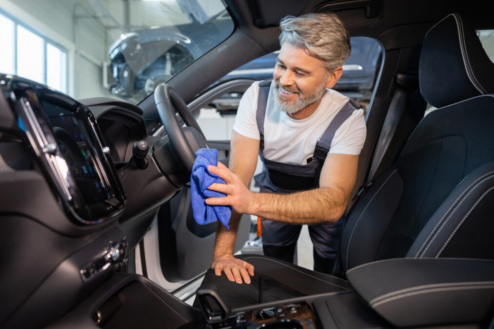 Car wash service. Bearded man worker cleaning automobile salon with rag