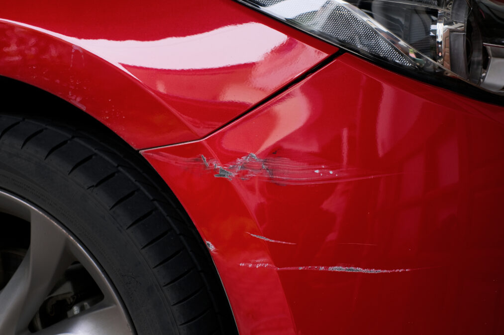 Red bumper car scratched with deep damage to the paint, accident concept.